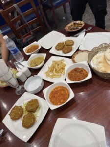 breakfast table with the food. Falafel, fries, a few dishes with a red sauce