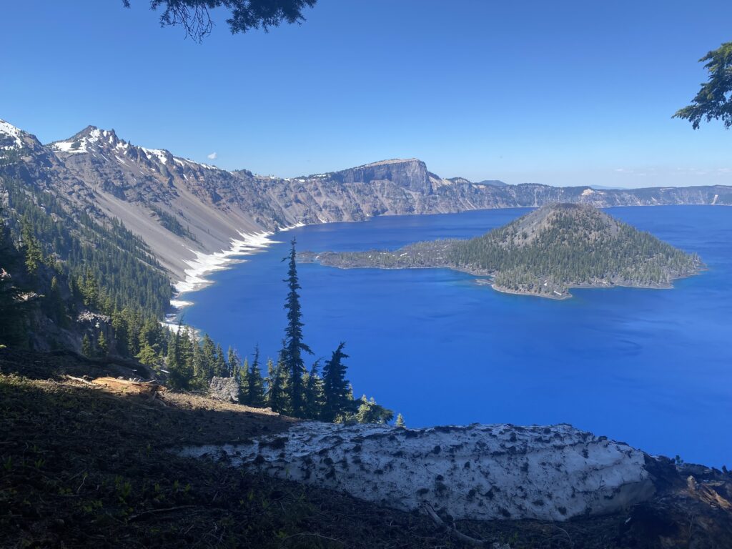 Crater lake. A deep blue big circle of water with a small island hill towards the left. The lake is surrounded by mountains (it is in a crater type area)