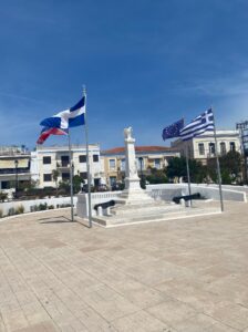 column (potentially a memorial) with an eagle on top and greek flags flowing in the wind next to it