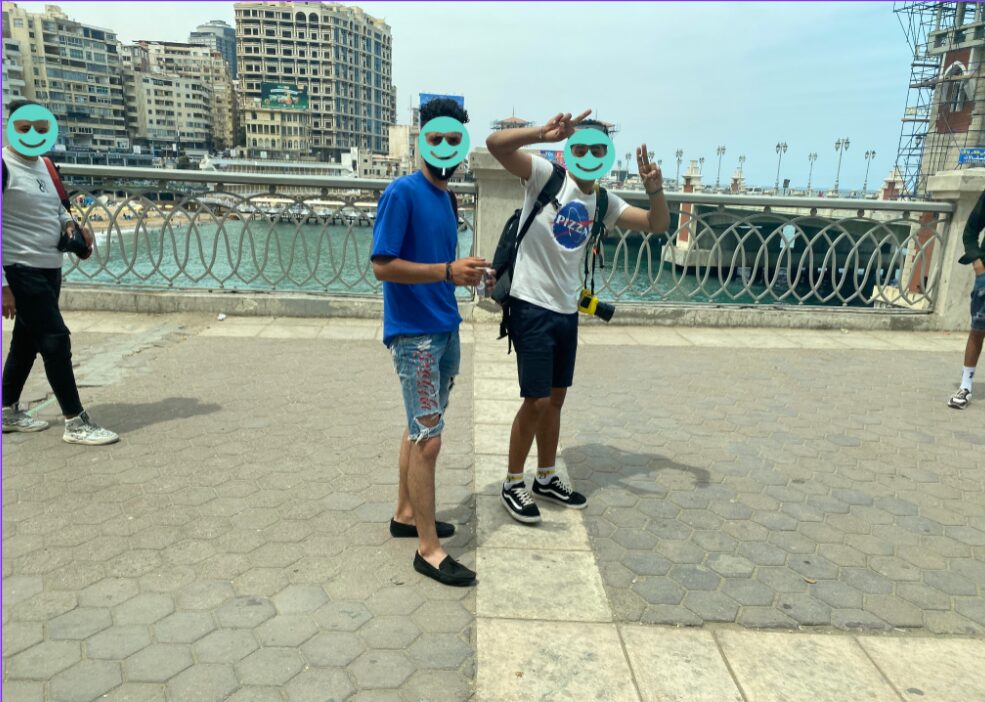 2 men photobombing a photo we were trying to take of the city from a bridge. on eod the men is holding up double peace signs and smirking. I have covered their faces with smiley faces