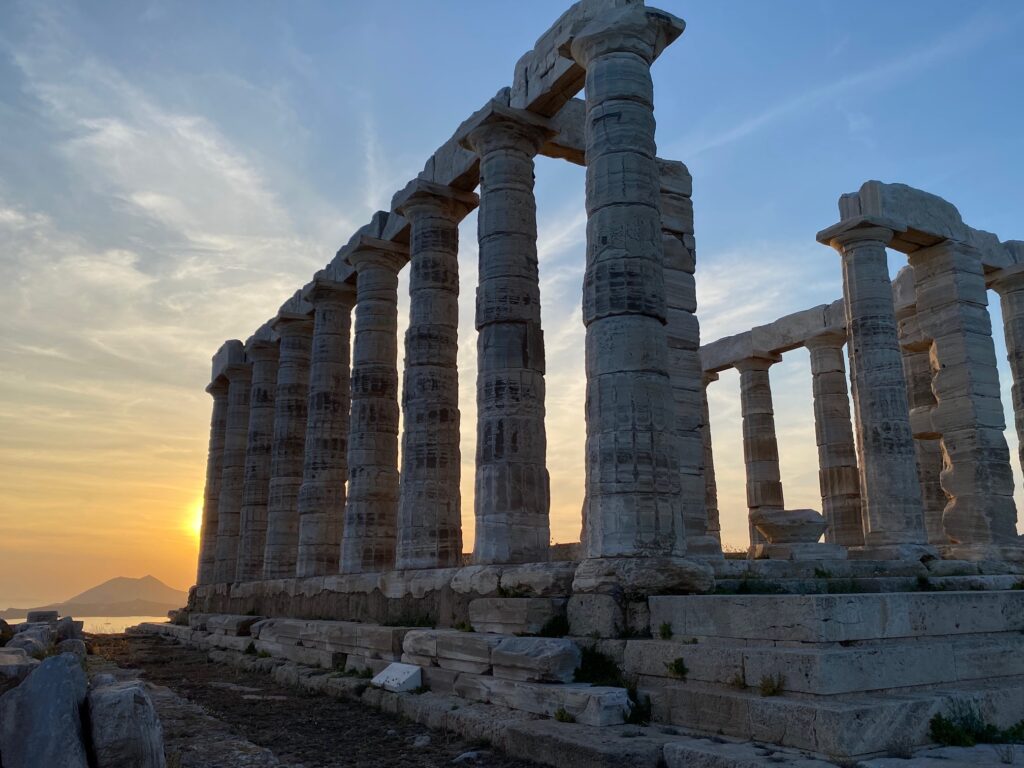 close up view of poseidon's temple from the bottom (the temple is old stone columns almost in a rectangle shape though not all is there). sunset in the background